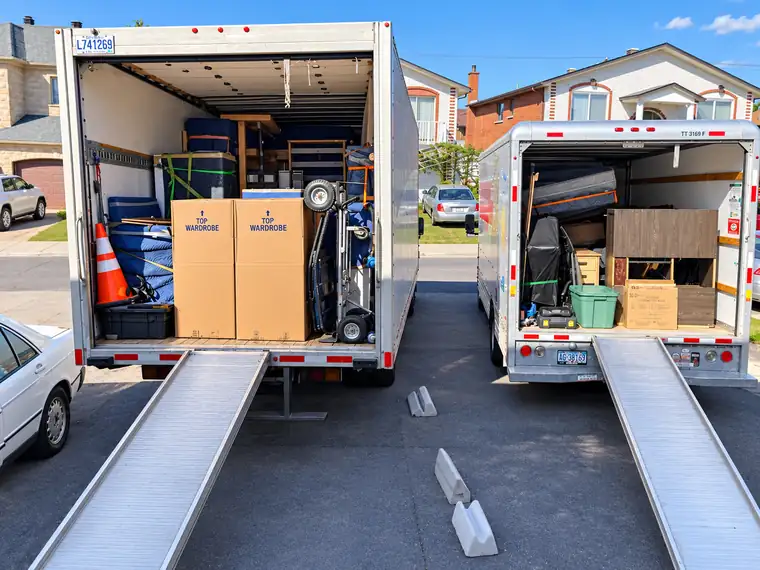 Deux camions de déménagement ouverts, rampes baissées et chargés de boîtes garde-robe et de matériel, prêts pour un déménagement de dernière minute