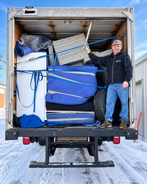 Déménageur Bon Avenir debout dans un camion chargé de meubles protégés par des couvertures, prêt pour un déménagement de dernière minute