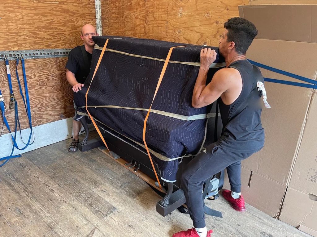 Bon Avenir movers securing a piano wrapped in moving blankets and straps inside the moving truck